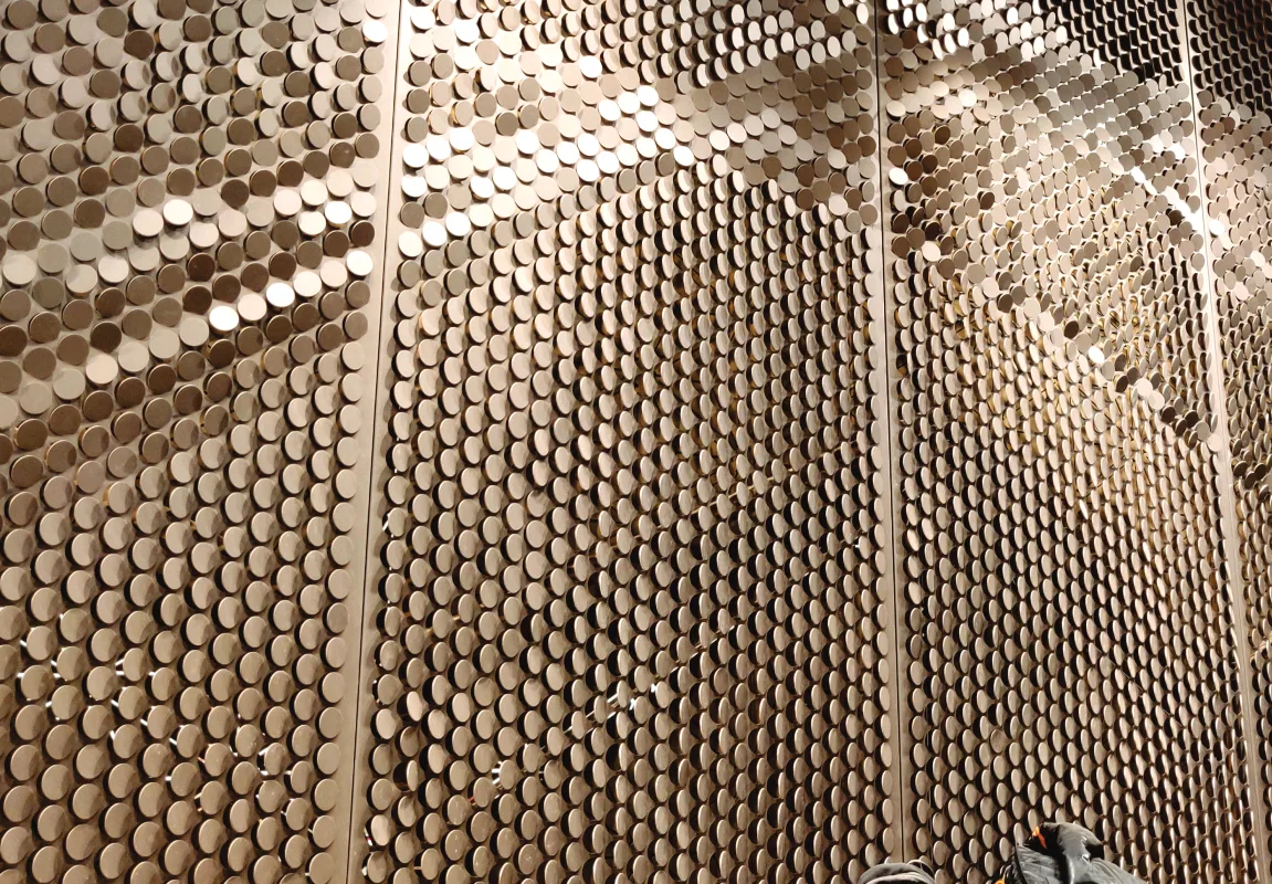 Brass coin matrix façade catching raking light